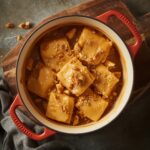 Golden caramel fudge cubes served in a red casserole dish, topped with crushed nuts, creating a rich and glossy homemade dessert.