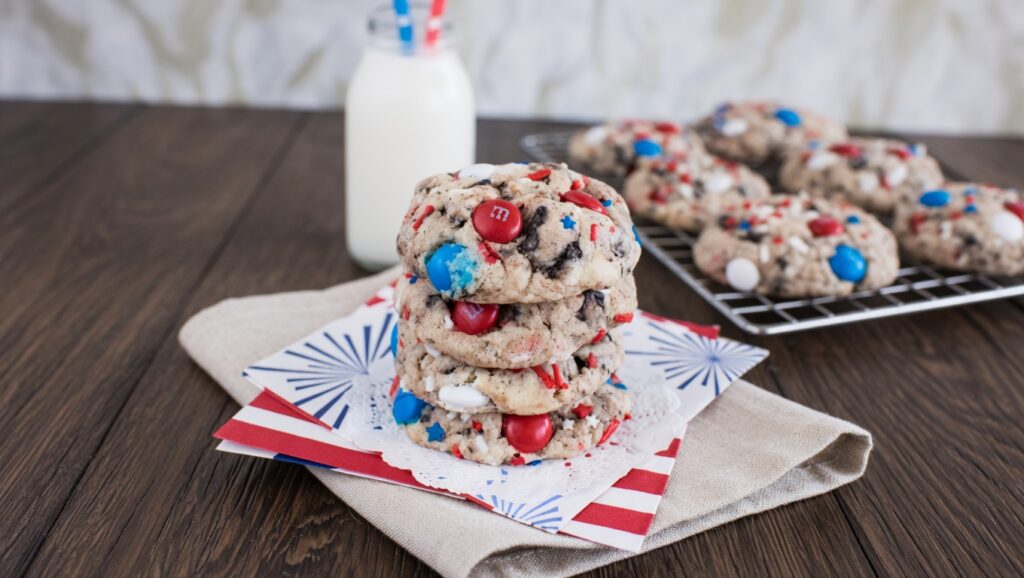 4th of July Cookies stacked on a white plate with red white and blue MandMs star sprinkles and Oreo chunks visible on a festive table