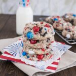 4th of July Cookies stacked on a white plate with red white and blue MandMs star sprinkles and Oreo chunks visible on a festive table