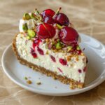 Cherry Pistachio Cheesecake on a white cake stand with glossy red cherry topping and crushed green pistachio garnish on marble surface