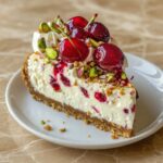 Slice of Cherry Pistachio Cheesecake on a white plate showing three distinct layers of golden crust creamy pistachio filling and vibrant cherry topping