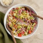 Italian Chopped Brussels Sprouts Salad in a large white bowl with salami olives chickpeas provolone and pepperoncini on a wooden table