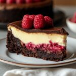 Raspberry Brownie Cheesecake on a white cake stand showing fudgy brownie base creamy filling and fresh raspberries on top
