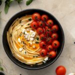 Roasted tomato and garlic ricotta pasta in a white bowl with fresh basil and Parmesan