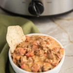 Tortilla chip being dipped into creamy slow cooker queso dip with ground beef