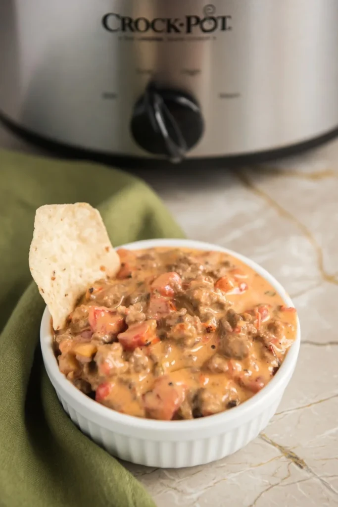 Tortilla chip being dipped into creamy slow cooker queso dip with ground beef