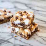 S'mores Cookie Bars stacked on a rustic wooden board with gooey marshmallow and melted chocolate chips visible on golden tops
