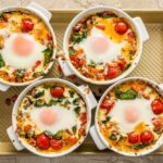 Baked Feta Eggs in a white ceramic ramekin with burst roasted cherry tomatoes wilted spinach creamy feta and fresh chives on a linen napkin
