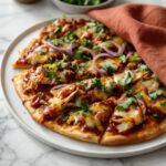 BBQ chicken flatbread with melted cheese, red onion, and fresh cilantro on a wooden board