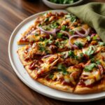 BBQ chicken flatbread being assembled with shredded chicken and cheese on a baking sheet