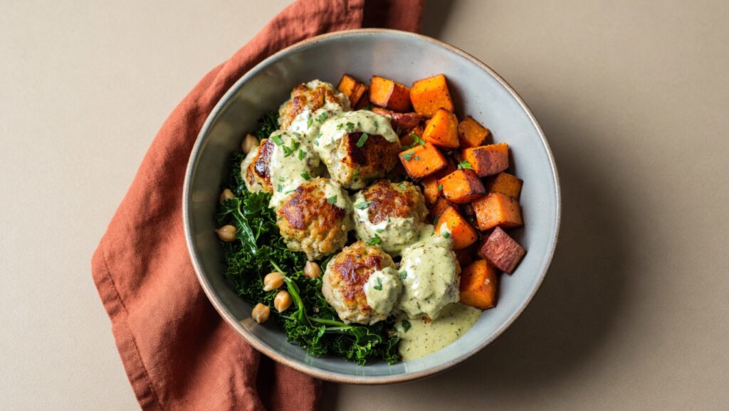 Herbed chicken meatball bowl with quinoa, fresh greens, cherry tomatoes, and balsamic dressing in a white bowl