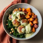 Herbed chicken meatball bowl with quinoa, fresh greens, cherry tomatoes, and balsamic dressing in a white bowl