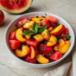 Easy Summer Peach Watermelon Salad in a wide white bowl with fresh mint leaves and lime wedge on a bright marble surface