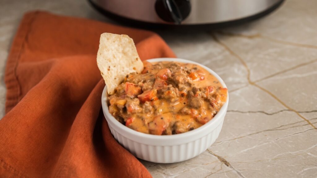 Slow cooker queso dip with ground beef and Rotel served with tortilla chips in a black crockpot