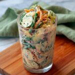 Viral Creamy Asian Cucumber Salad in a glass jar with thin cucumber slices shredded carrots edamame tofu and sesame seeds on a clean white surface